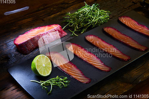 Image of Sliced salmon fillet, salted with beetroot juice, served on whole wheat with salad leaves, sea salt and pepper over metal surface. Top view