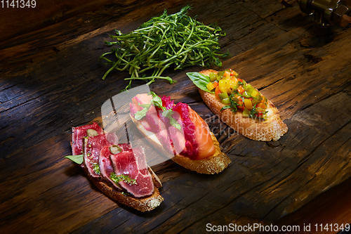 Image of Assorted bruschetta with roast beef, vegetables and lightly salted salmon with greens leaves on wooden background.