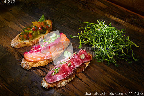 Image of Assorted bruschetta with roast beef, vegetables and lightly salted salmon with greens leaves on wooden background.