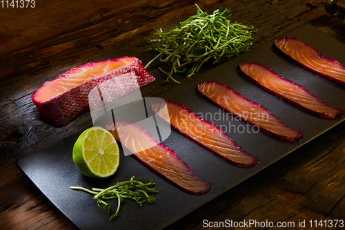Image of Sliced salmon fillet, salted with beetroot juice, served on whole wheat with salad leaves, sea salt and pepper over metal surface. Top view