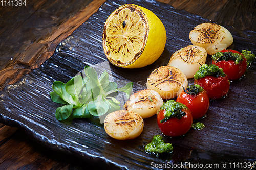 Image of Fried scallops with tomatoes on a black plate. Shallow dof.