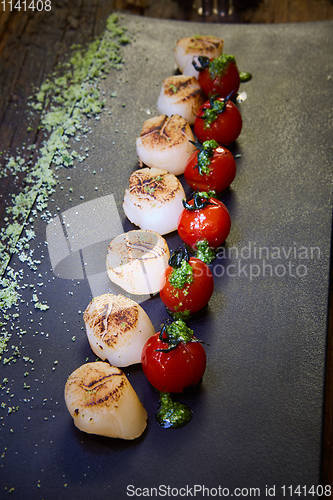 Image of Fried scallops with tomatoes on a black plate. Shallow dof.