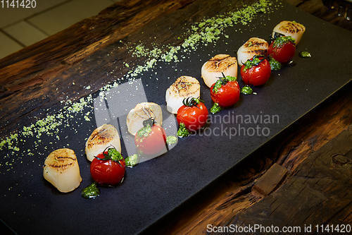 Image of Fried scallops with tomatoes on a black plate. Shallow dof.