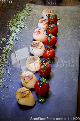 Image of Fried scallops with tomatoes on a black plate. Shallow dof.