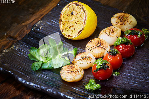 Image of Fried scallops with tomatoes on a black plate. Shallow dof.