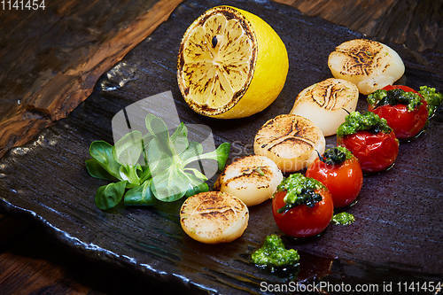 Image of Fried scallops with tomatoes on a black plate. Shallow dof.