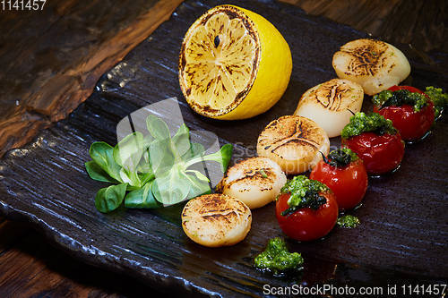 Image of Fried scallops with tomatoes on a black plate. Shallow dof.