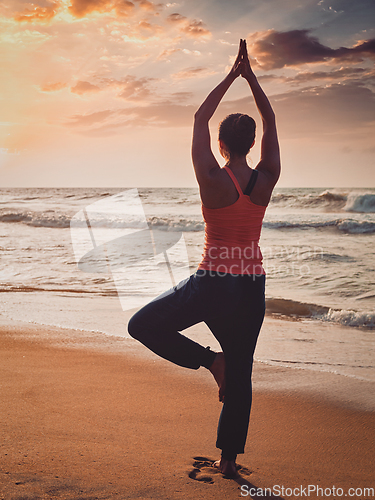 Image of Young sporty fit woman doing yoga tree asana on beach