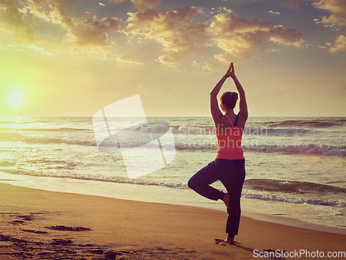 Image of Young sporty fit woman doing yoga tree asana on beach