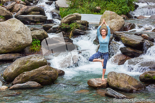 Image of Woman in yoga asana Vrikshasana tree pose at waterfall outdoors