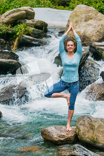 Image of Woman in yoga asana Vrikshasana tree pose at waterfall outdoors