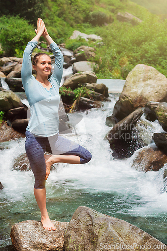 Image of Woman in yoga asana Vrikshasana tree pose at waterfall outdoors