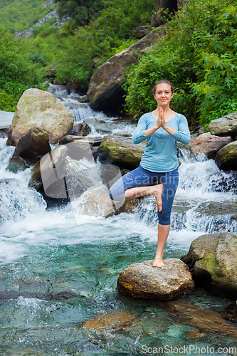 Image of Woman in yoga asana Vrikshasana tree pose at waterfall outdoors