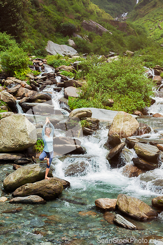 Image of Woman in yoga asana Vrikshasana tree pose at waterfall outdoors