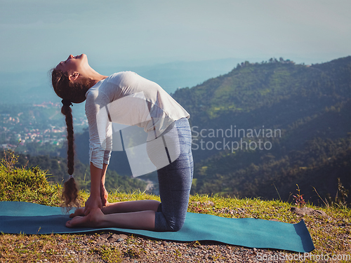 Image of Woman doing yoga asana Ustrasana camel pose outdoors