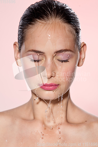 Image of Beautiful Model Girl with splashes of water on her face. Beautiful Woman under splash of water with fresh skin over pink background. Skin care Cleansing and moisturizing concept. Beauty face
