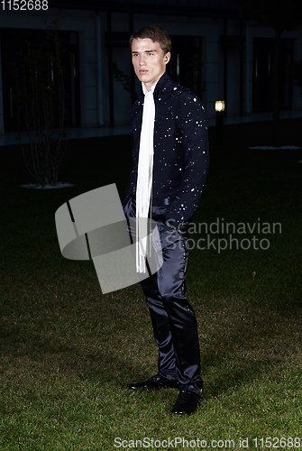 Image of Male fashion, beauty concept. Portrait of young man with short wet hair wearing black suit, posing on street. Classic style.