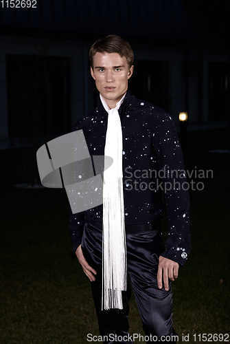 Image of Male fashion, beauty concept. Portrait of young man with short wet hair wearing black suit, posing on street. Classic style.