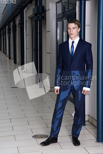 Image of Portrait of an attractive young businessman in urban background wearing blue suit and necktie. Looking to the camera. Classic style.