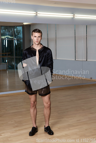 Image of Man in elegant suite posing in fitness gym. High fashion young sexy man in black shorts and a black jacket