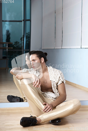 Image of Man in elegant sport suit posing in fitness gym. Young man in gold sport leggings