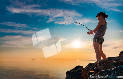 Image of Woman fishing on Fishing rod spinning at sunset background.