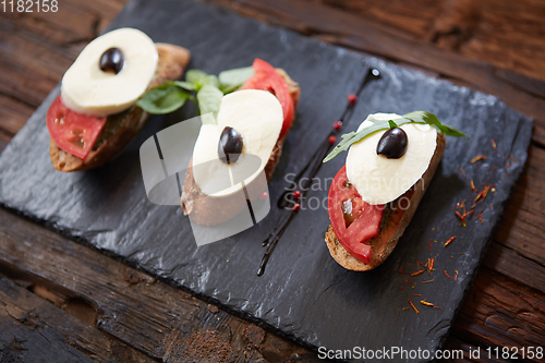 Image of Italian bruschetta with chopped tomatoes, basil, mozzarella cheese and balsamic vinegar. Fresh homemade caprese bruschetta or crostini over black stone background, copy space.