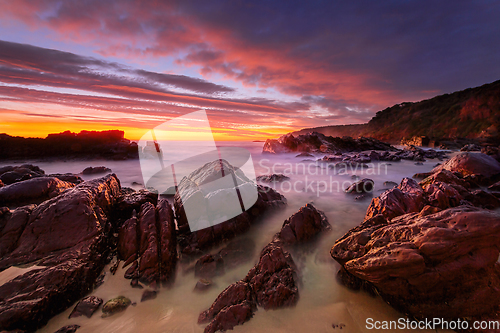 Image of Vivid red sunrise over rocky beach coast