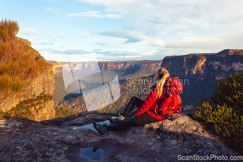 Image of Woman sits at cliff edge and takes in magnificent mountain views