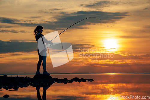 Image of Woman fishing on Fishing rod spinning at sunset background.