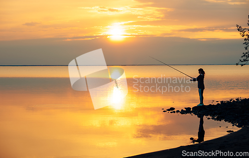 Image of Woman fishing on Fishing rod spinning at sunset background.