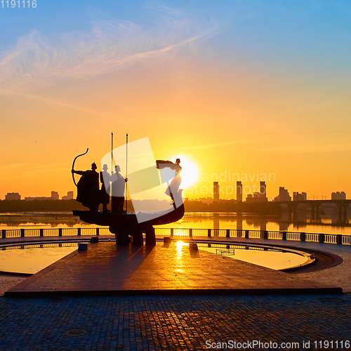 Image of Monument to the founders of Kyiv at sunrise, wide-angle view with blue sky and yellow sun. Statue of Kyi, Shchek, Horyv and Lybid.