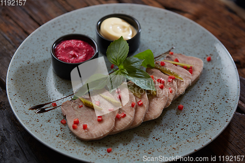 Image of Sliced cold baked pork with herbs on blue plate