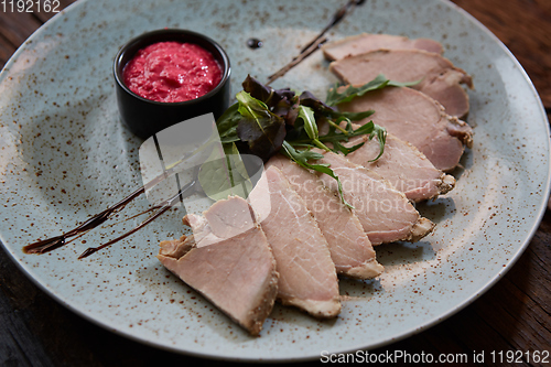 Image of Sliced cold baked pork with herbs on blue plate