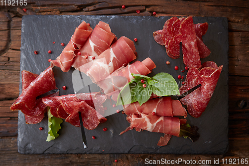 Image of Slices of Italian prosciutto crudo or jamon with fresh basil leaves on a black background.