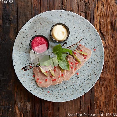 Image of Sliced cold baked pork with herbs on blue plate