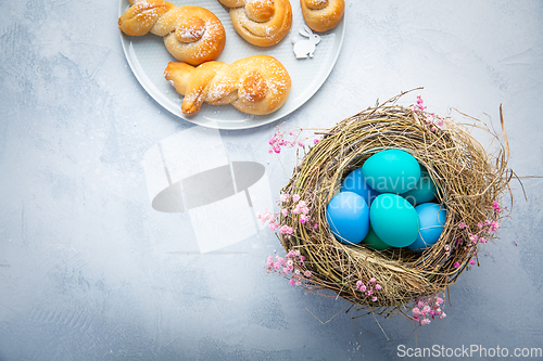 Image of Easter eggs in nest with sweet buns made from yeast dough in a s
