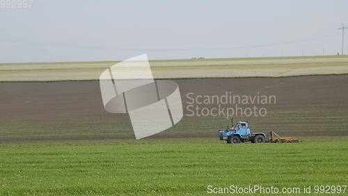 Image of Blue wheeled tractor plowing a green field