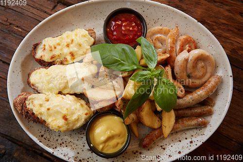 Image of Grilled assorted sausages with French fries, bruschettes with cheese and sauces.