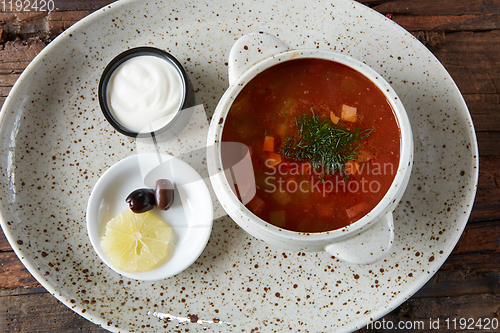 Image of Soup saltwort with lemon, meat, pickles, tomato sauce olives in a bowl on a sacking.