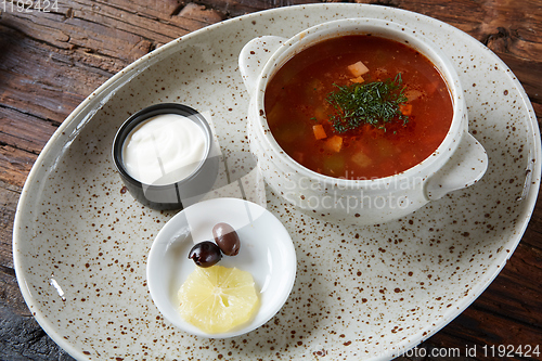 Image of Soup saltwort with lemon, meat, pickles, tomato sauce olives in a bowl on a sacking.