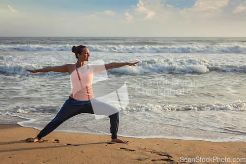 Image of Woman doing yoga asana Virabhadrasana 1 Warrior Pose on beach on