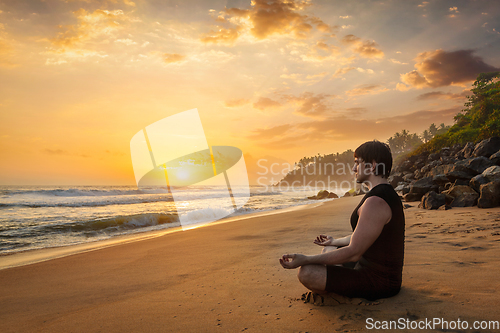 Image of Young sporty fit man doing yoga meditating on tropical beach