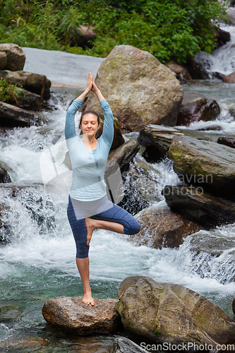 Image of Woman in yoga asana Vrikshasana tree pose at waterfall outdoors