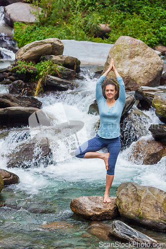 Image of Woman in yoga asana Vrikshasana tree pose at waterfall outdoors