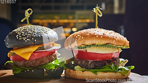 Image of Set of homemade burgers in black and white buns with tomato, lettuce, cheese, onion on wood serving board over dark table. Rustic style. Homemade fast food.