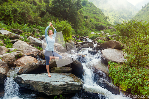 Image of Woman in yoga asana Vrikshasana tree pose at waterfall outdoors