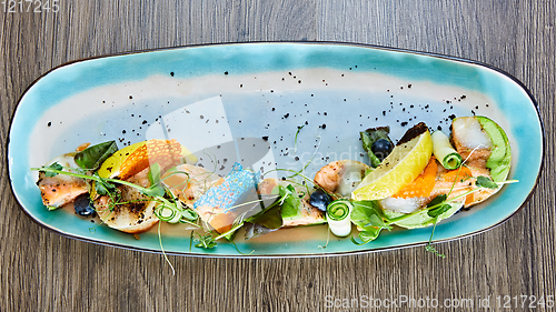 Image of fried fish rolls with herbs and vegetables on blue plate.