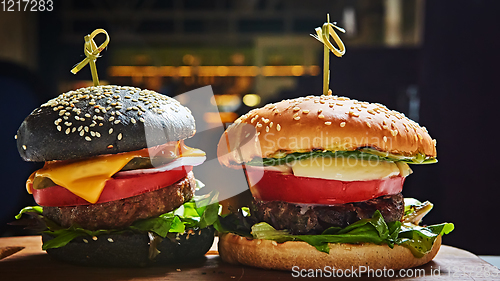 Image of Set of homemade burgers in black and white buns with tomato, lettuce, cheese, onion on wood serving board over dark table. Rustic style. Homemade fast food.