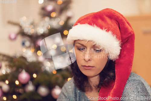Image of Beautiful middle age woman in santa hat sitting near the Christmas tree